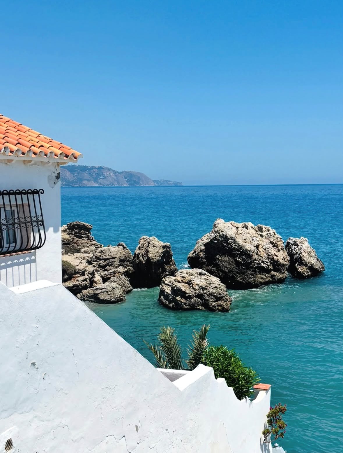 Whitewashed coastal building above rocks and clear blue water