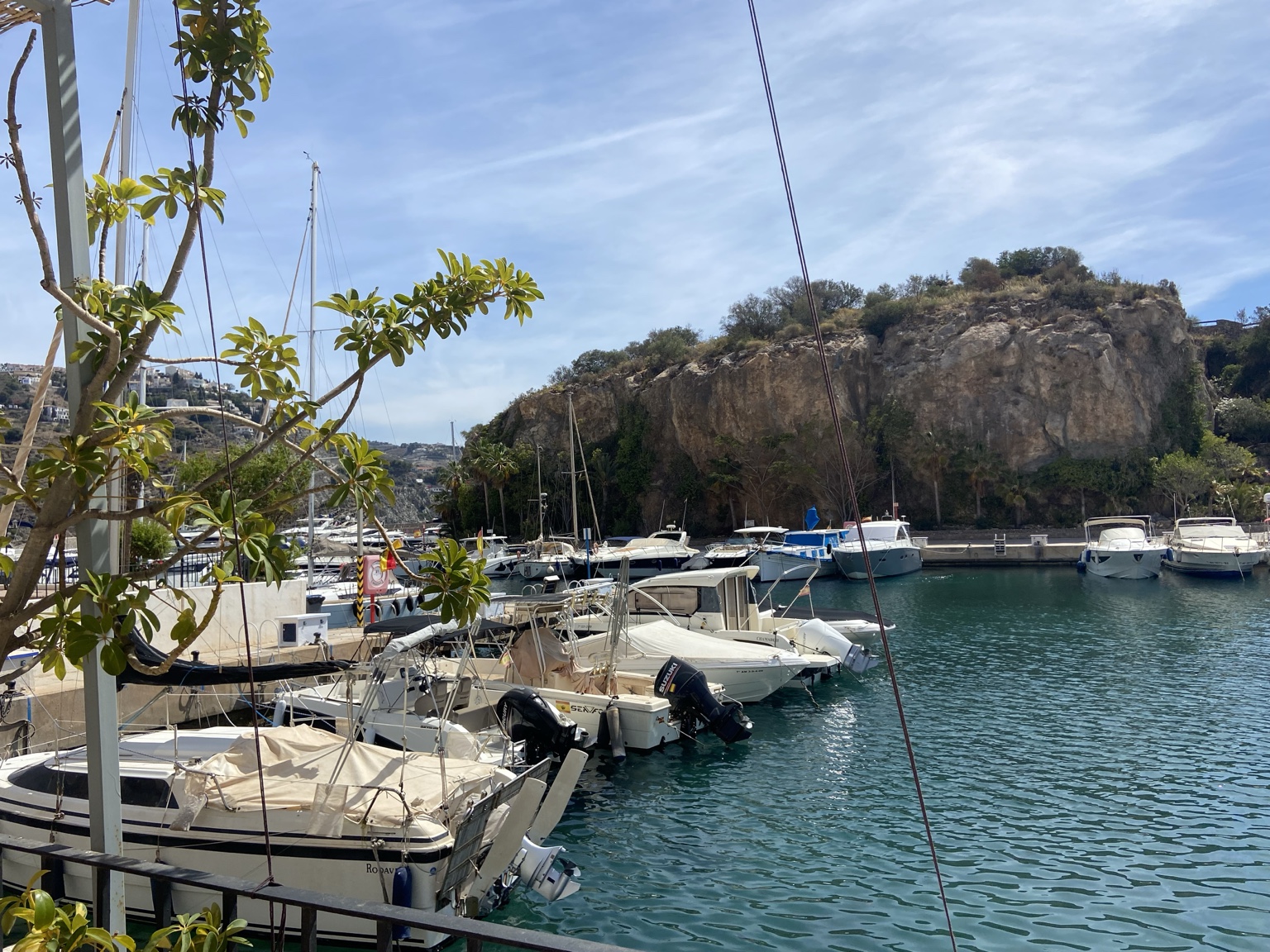 Boats moored in turquoise marina water beneath a rocky headland